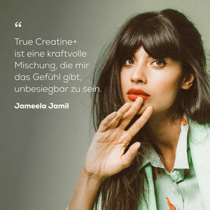 A woman with dark hair poses against a muted gray-green background. White German text on the left reads, 'True Creatine+ ist eine kraftvolle Mischung, die mir das Gefühl gibt, unbesiegbare zu sein.' Jameela Jamil.